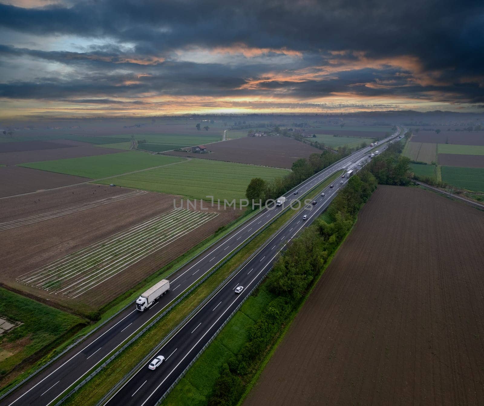 Cargo trucks and cars in the motorway a1 autostrada del sole aerial point of view in between padain plain rural fields