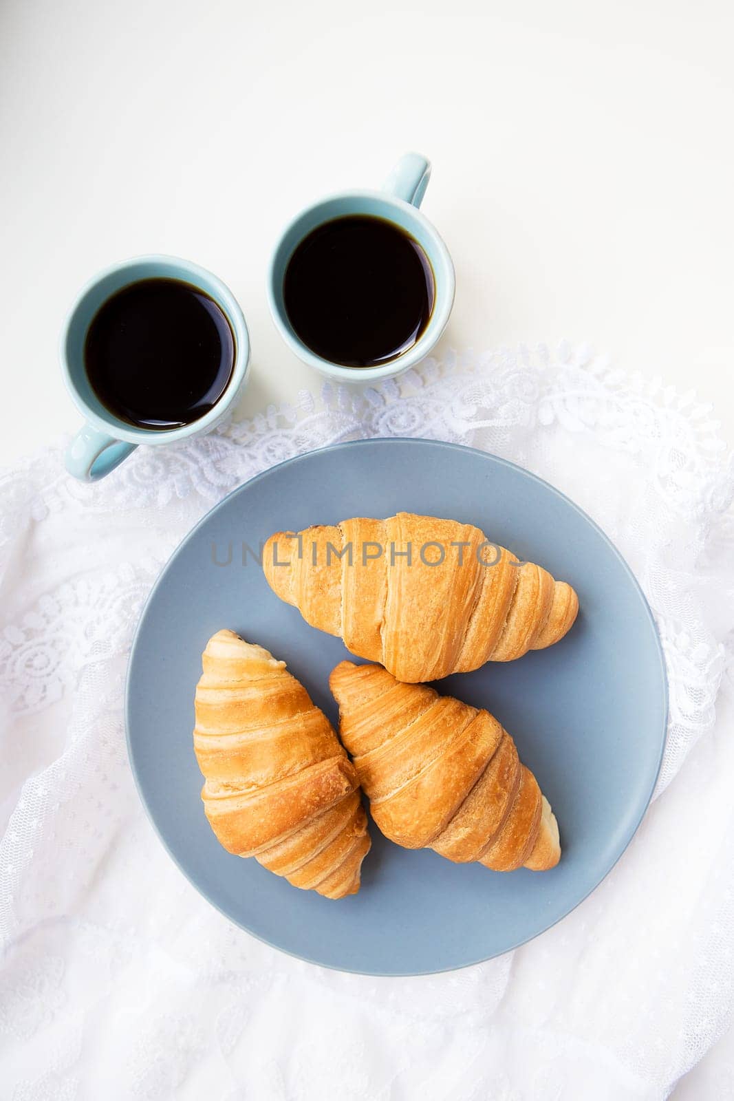 two cups of coffee with croissants on the background of laces on a white background