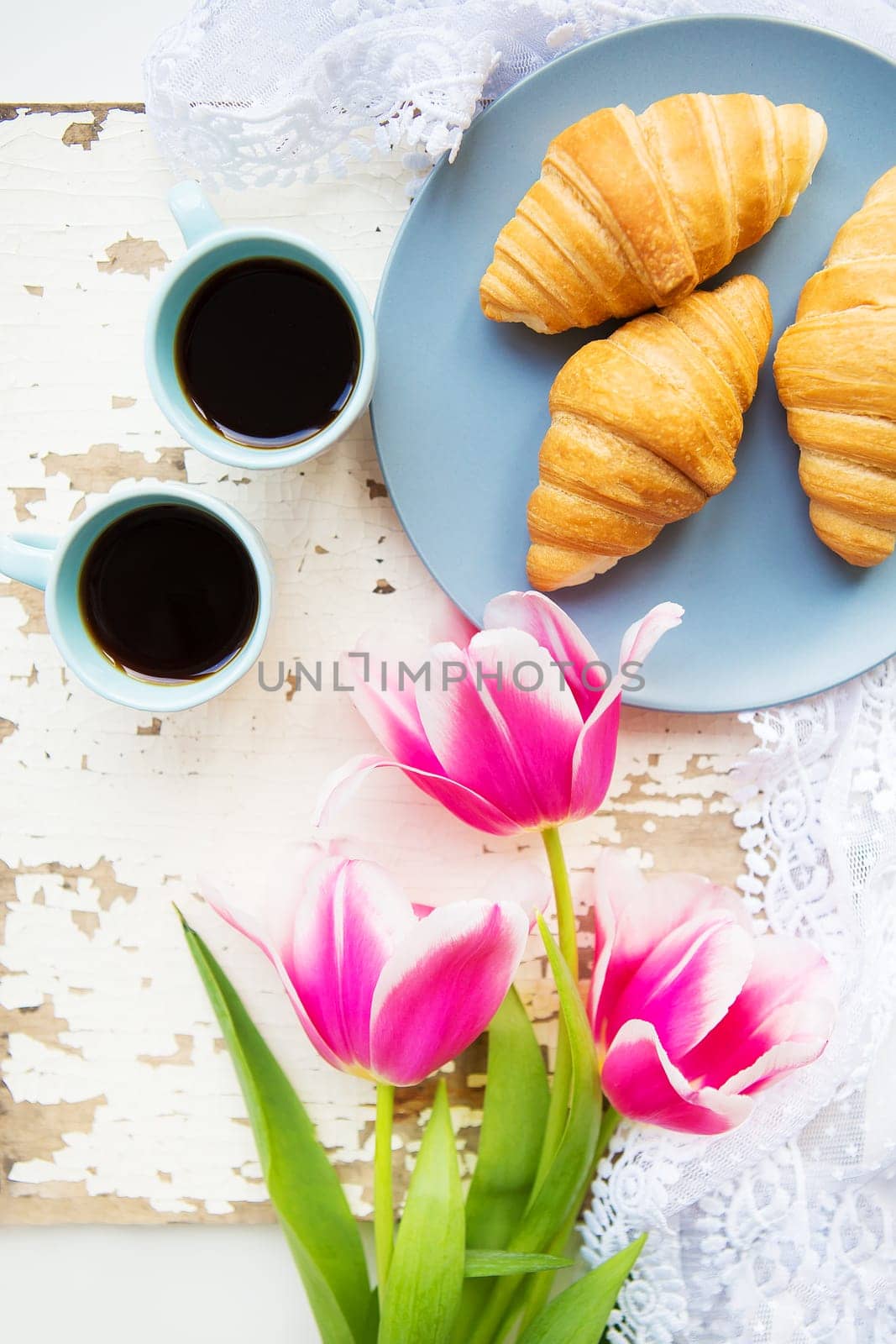 coffee, croissants and three beautiful pink tulips on old white table by sfinks