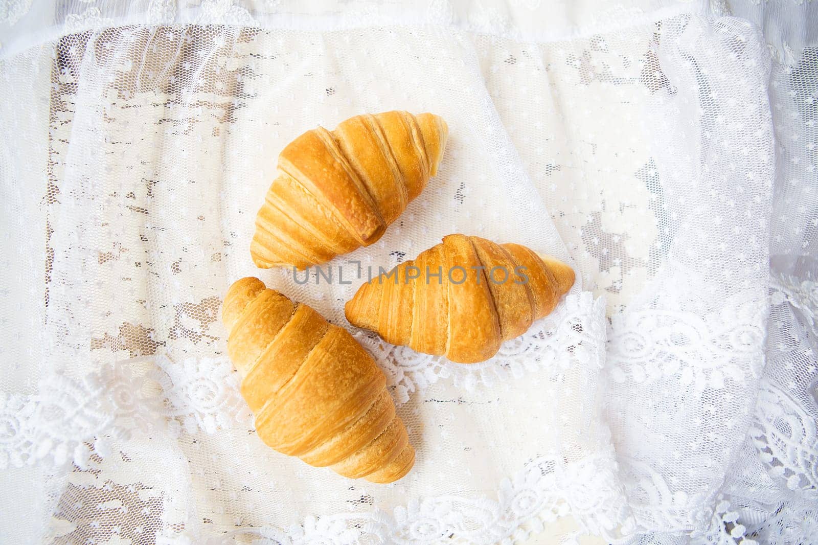 Beautiful and delicious croissants on the background of old laces and white table by sfinks