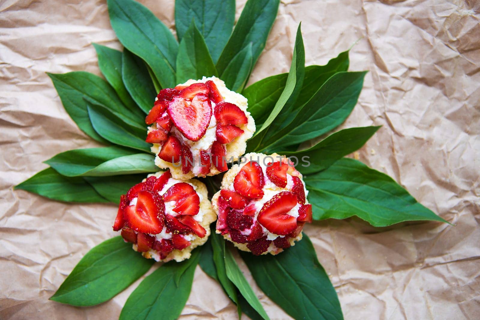 Beautiful and bright cupcakes with strawberries lie on green leaves, close-up.