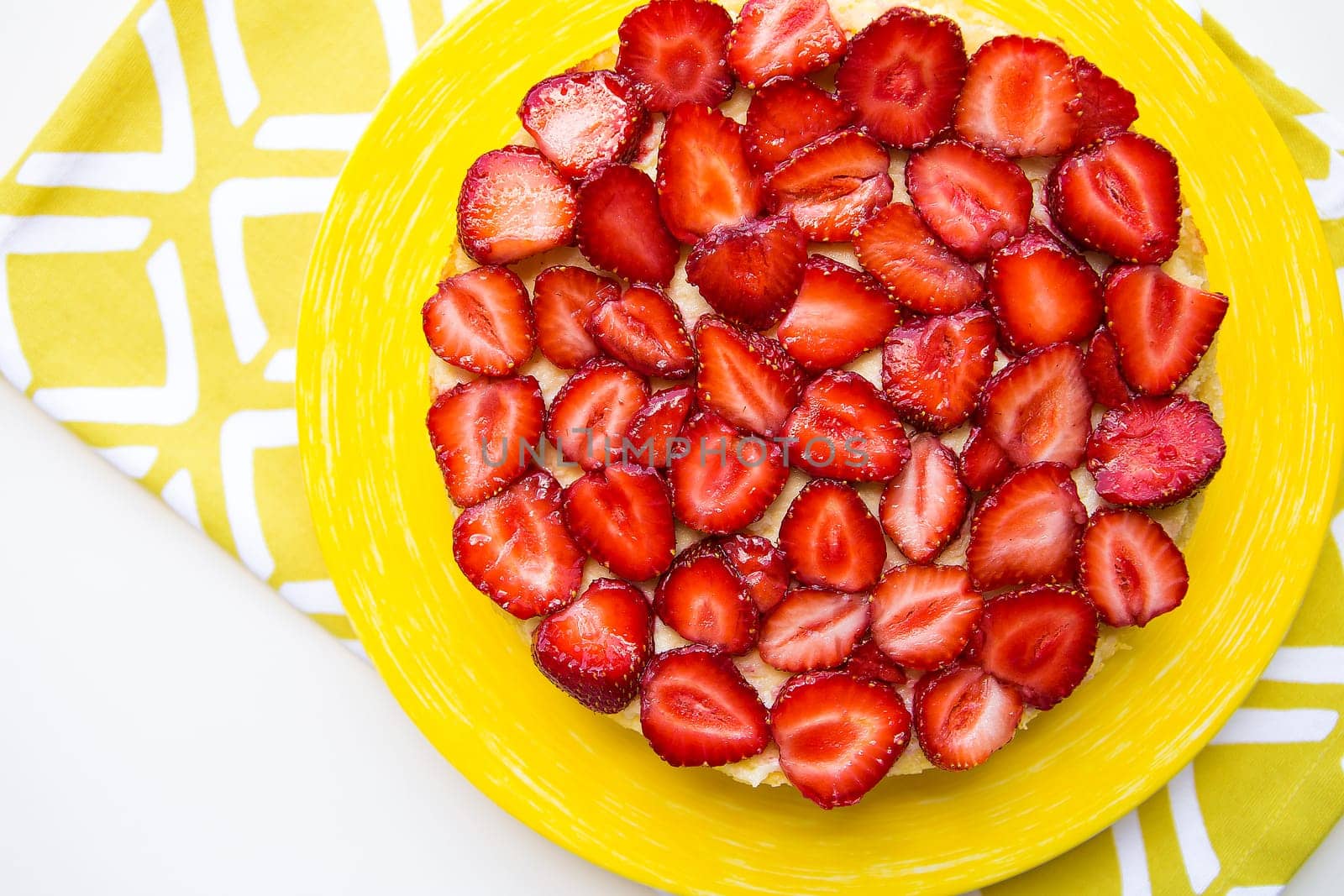 Beautiful and delicious strawberry cake stands on a yellow napkin.