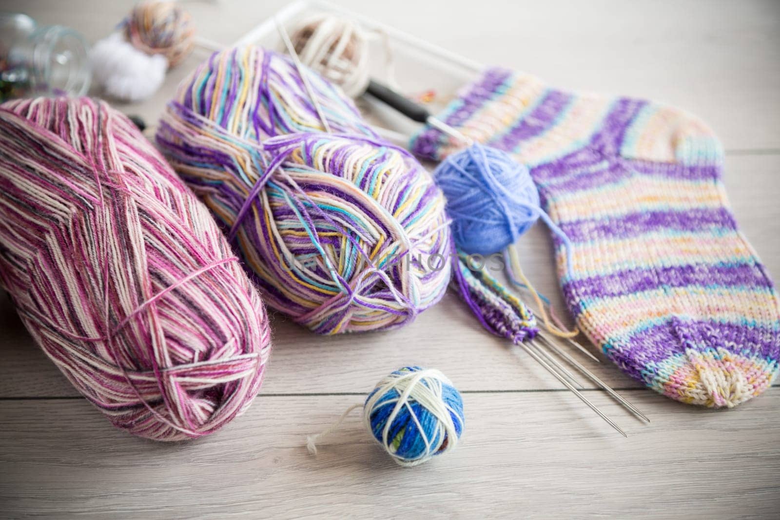 Colored threads, knitting needles and other items for hand knitting, on a light wooden table .