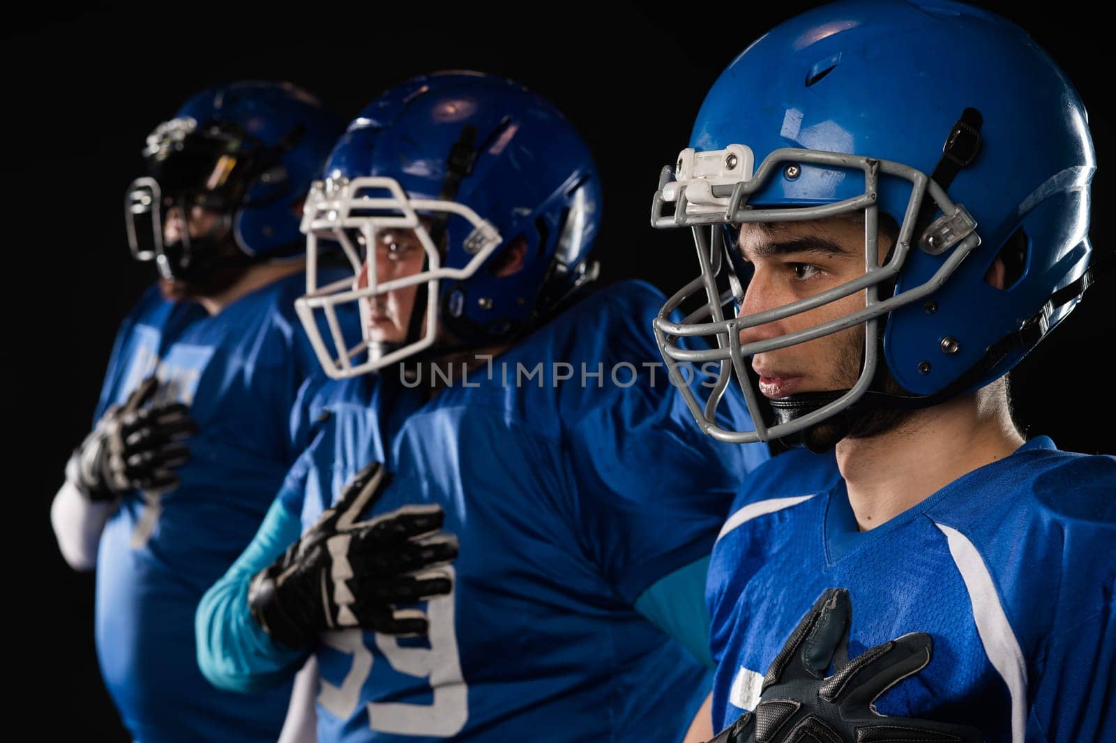 Portrait of three men in blue uniforms for American football with a hand on his chest on a black background