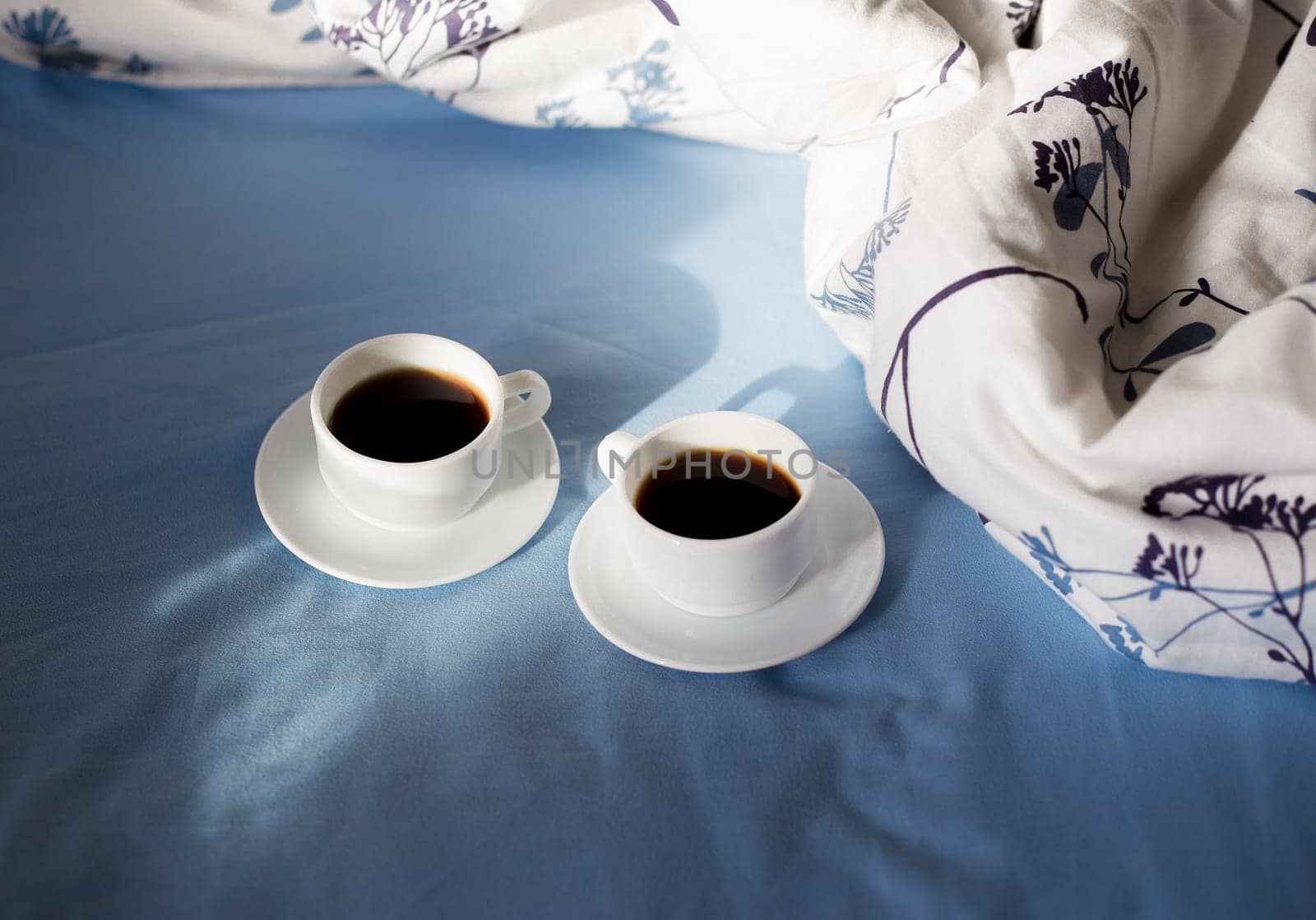 Two white cups of coffee are in bed, sunny morning by sfinks