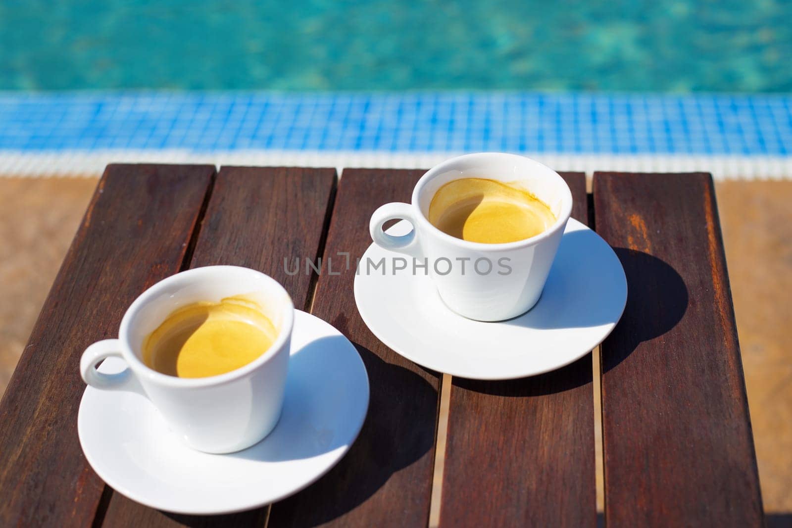 Two cups of coffee on the table near the pool. by sfinks