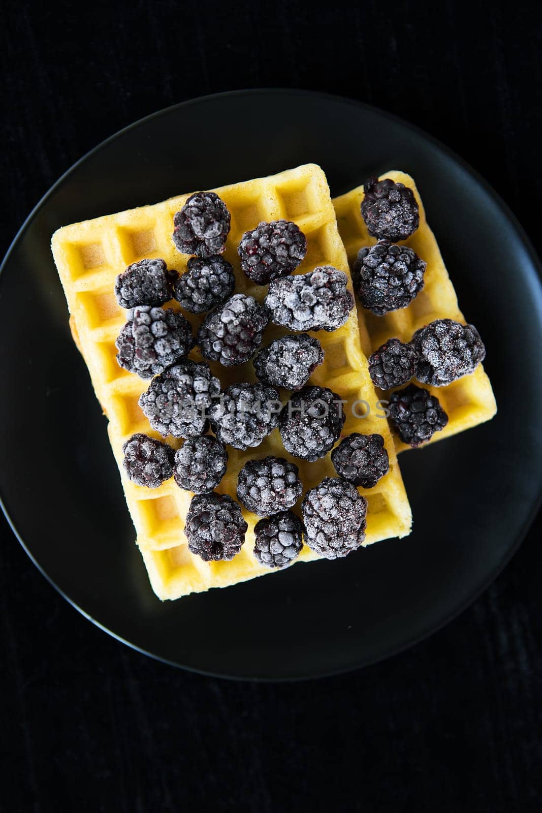 Belgian wafers with frozen blackberries on a black background.