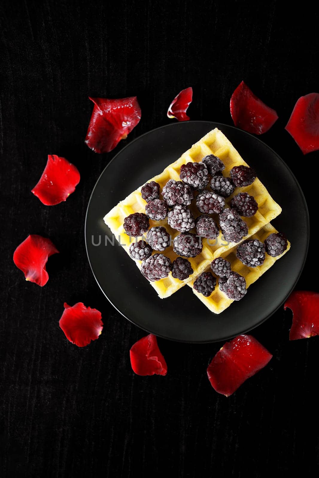 Belgian waffles with blackberries on a black background with petals of roses. valentine card