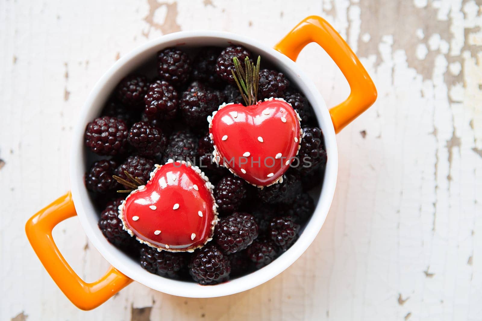 A full blackberry plate with a dessert in the form of a heart stands on a wooden background, close-up. valentine card