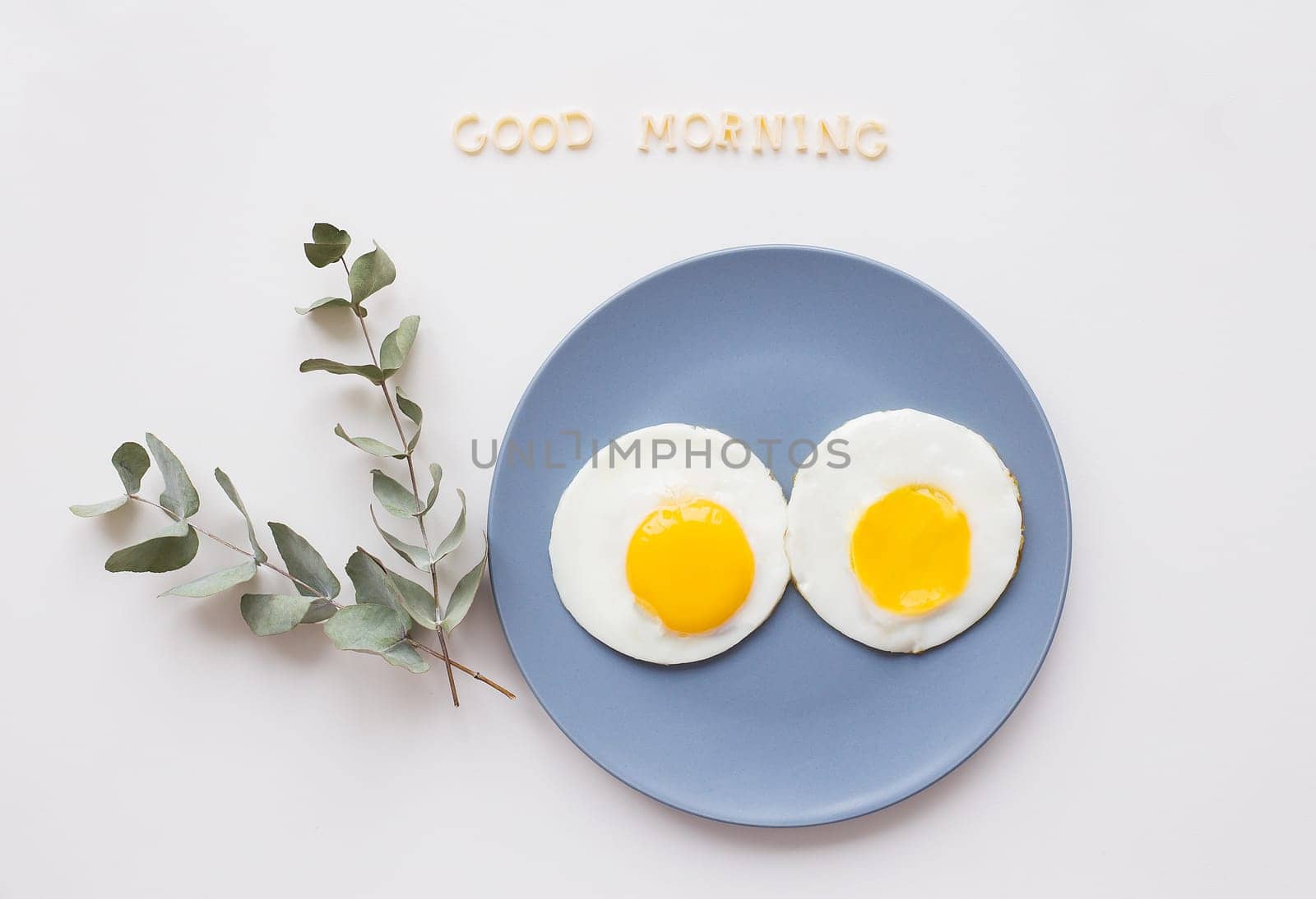 two eggs on a plate with a sprig of eucalyptus, an inscription good morning