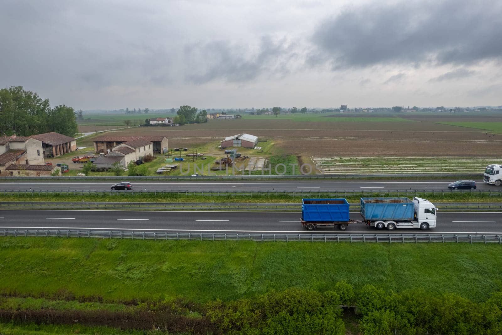 Piacenza, Italy - April 2023 Cargo trucks and cars in the motorway a1 autostrada del sole aerial point of view in between padain plain rural fields