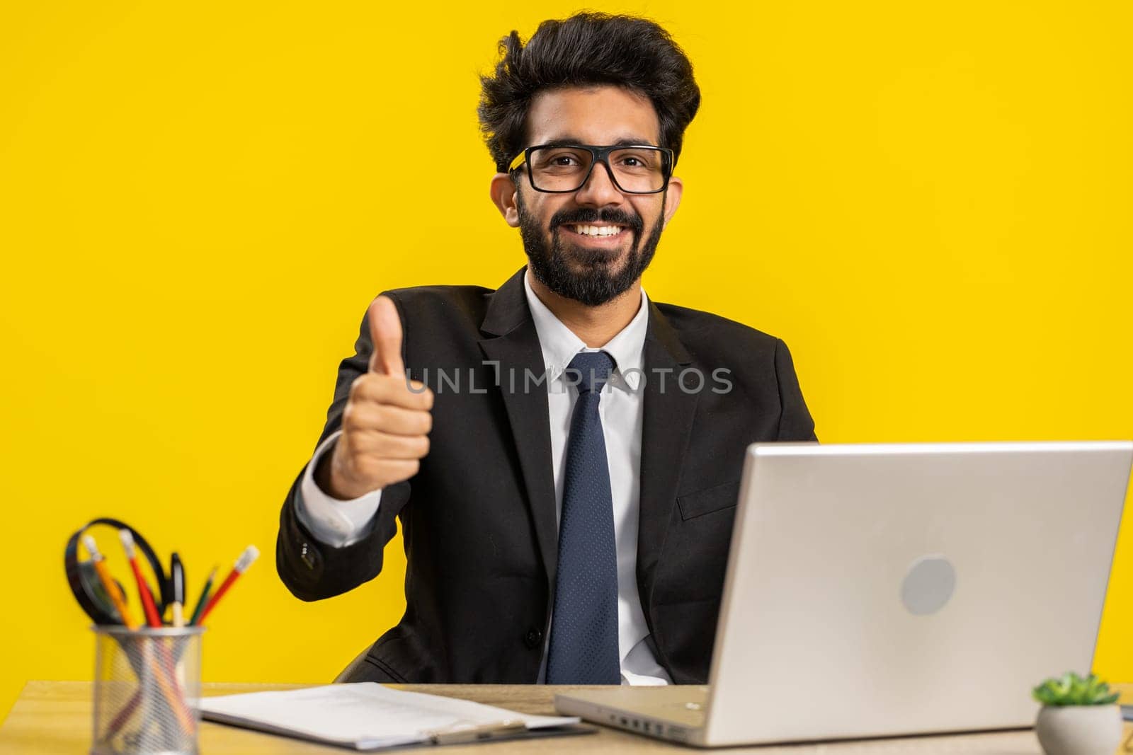Like. Happy young indian businessman guy working on laptop looking approvingly at camera showing thumbs up, like sign positive something good, positive feedback at office workplace. Freelancer man