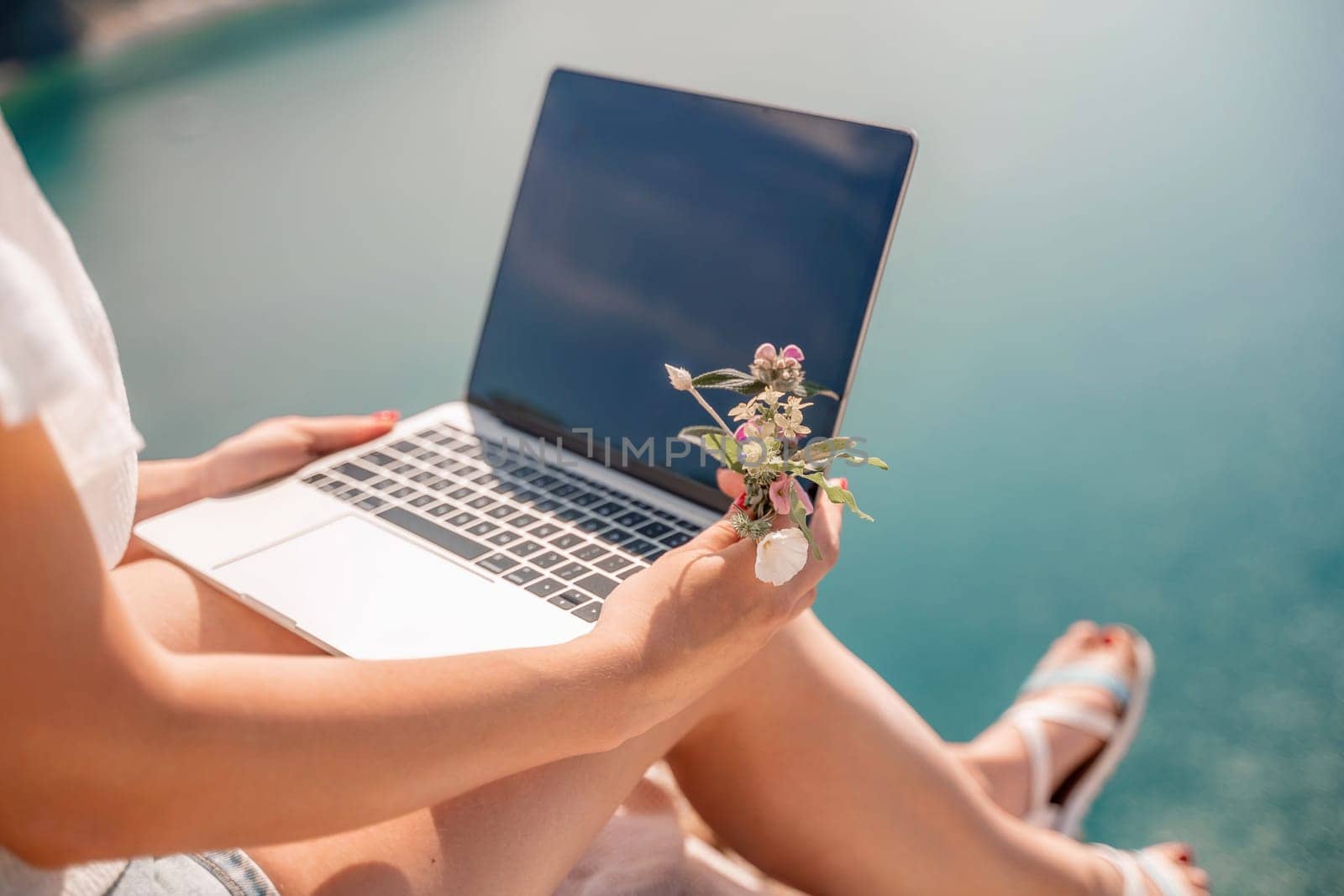 Freelance woman working on a laptop by the sea, typing away on the keyboard while enjoying the beautiful view, highlighting the idea of remote work