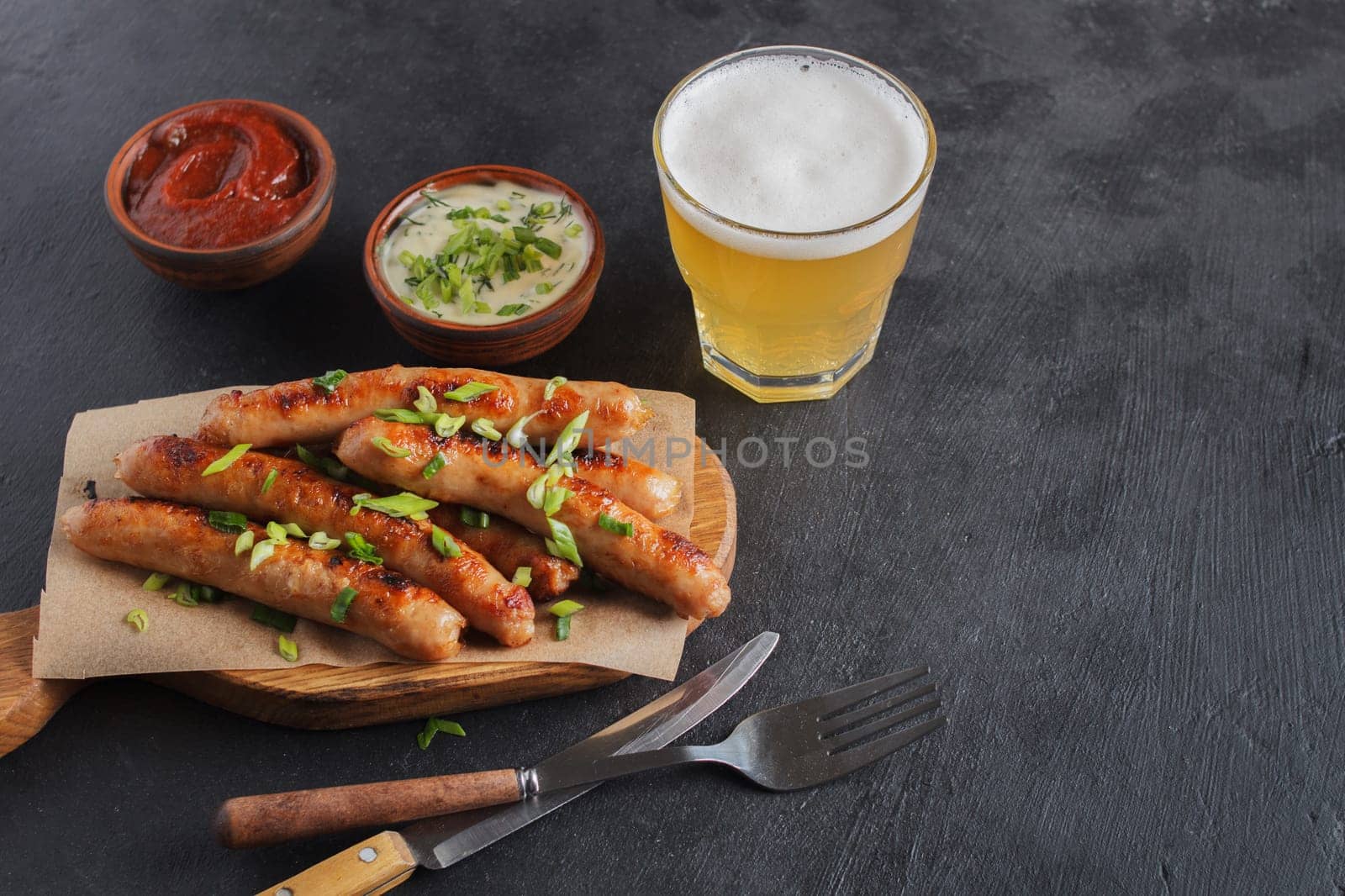 Tasty sausages on a wooden board with various sauces with a glass of beer on a black background. copy space.