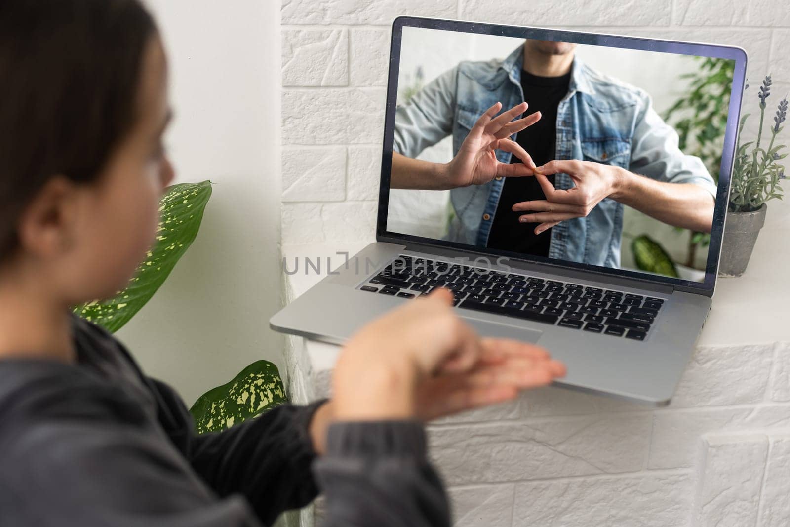 Distant education. Friendly teen girl having online lesson via laptop and showing gesturing in sign language, studying online from home by Andelov13