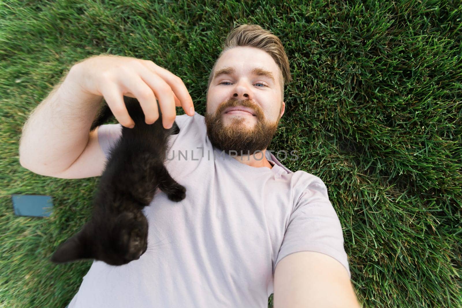 Man taking selfie with smartphone with little kitten lying and playing on grass - friendship love animals and pet owner concept by Satura86