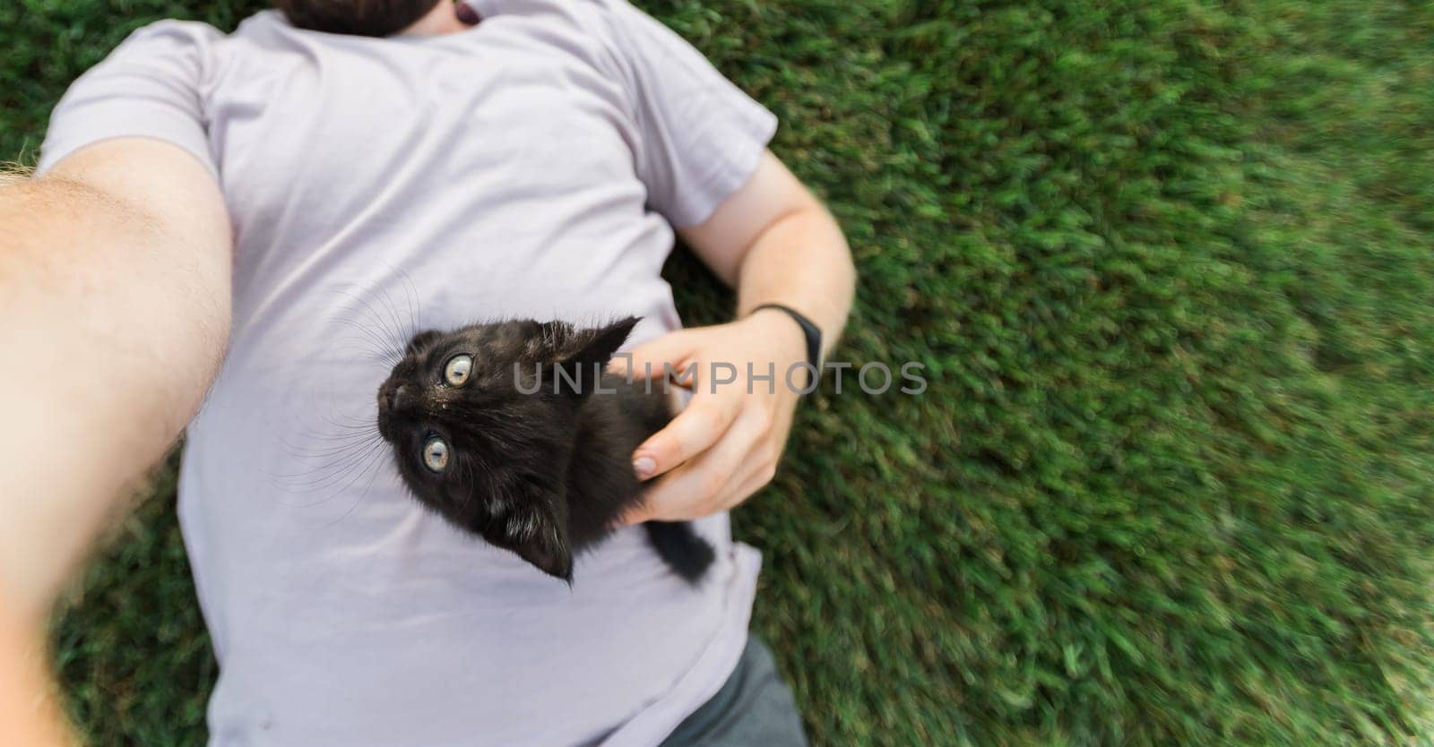 Man with little kitten lying and playing on grass - friendship love animals and pet owner