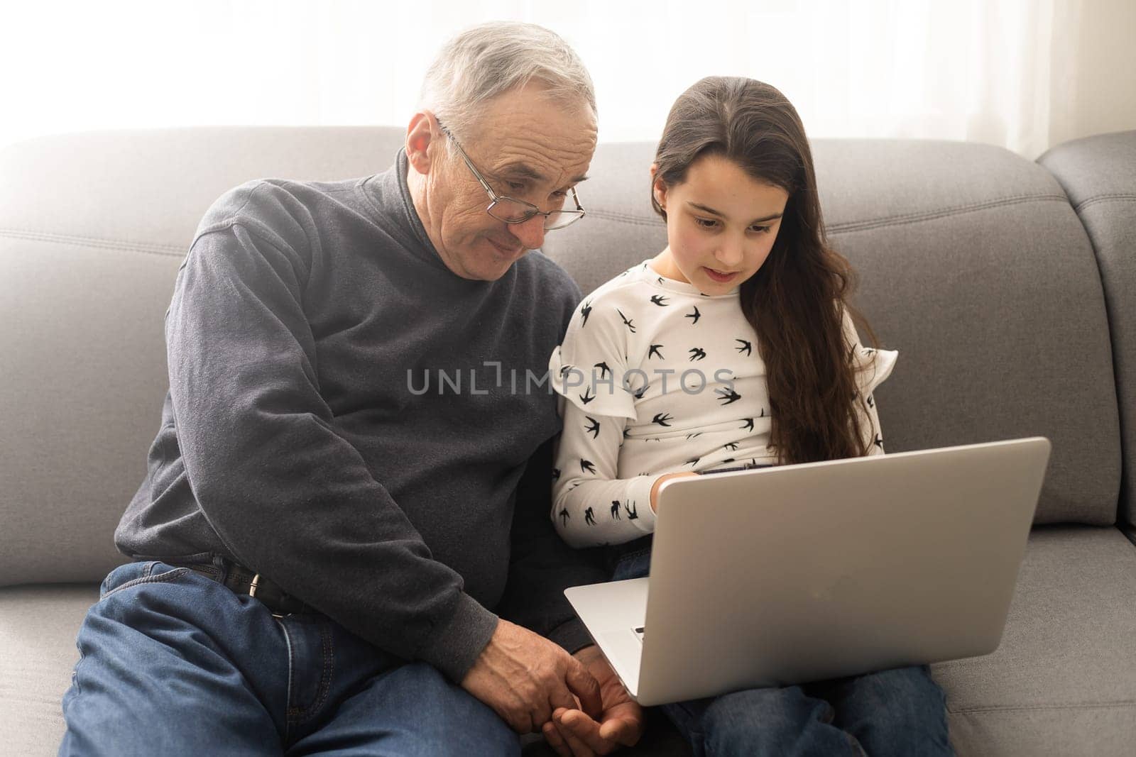 Adorable little girl and happy grandfather using laptop at home.