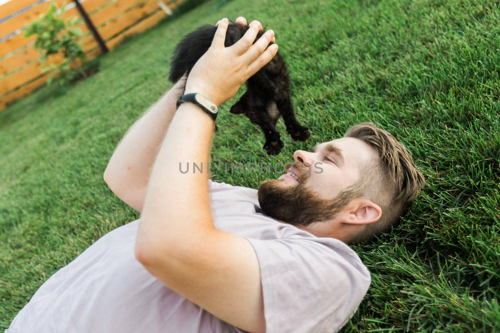 Man with little kitten lying and playing on grass - friendship love animals and pet owner