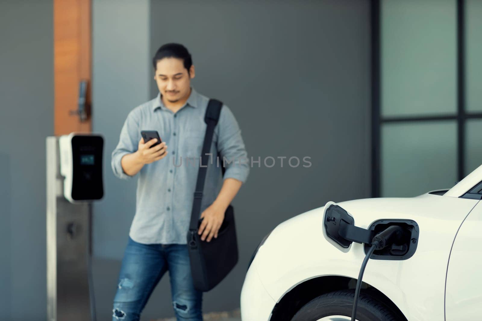 Progressive asian man and electric car with home charging station. Concept of the use of electric vehicles in a progressive lifestyle contributes to a clean and healthy environment.