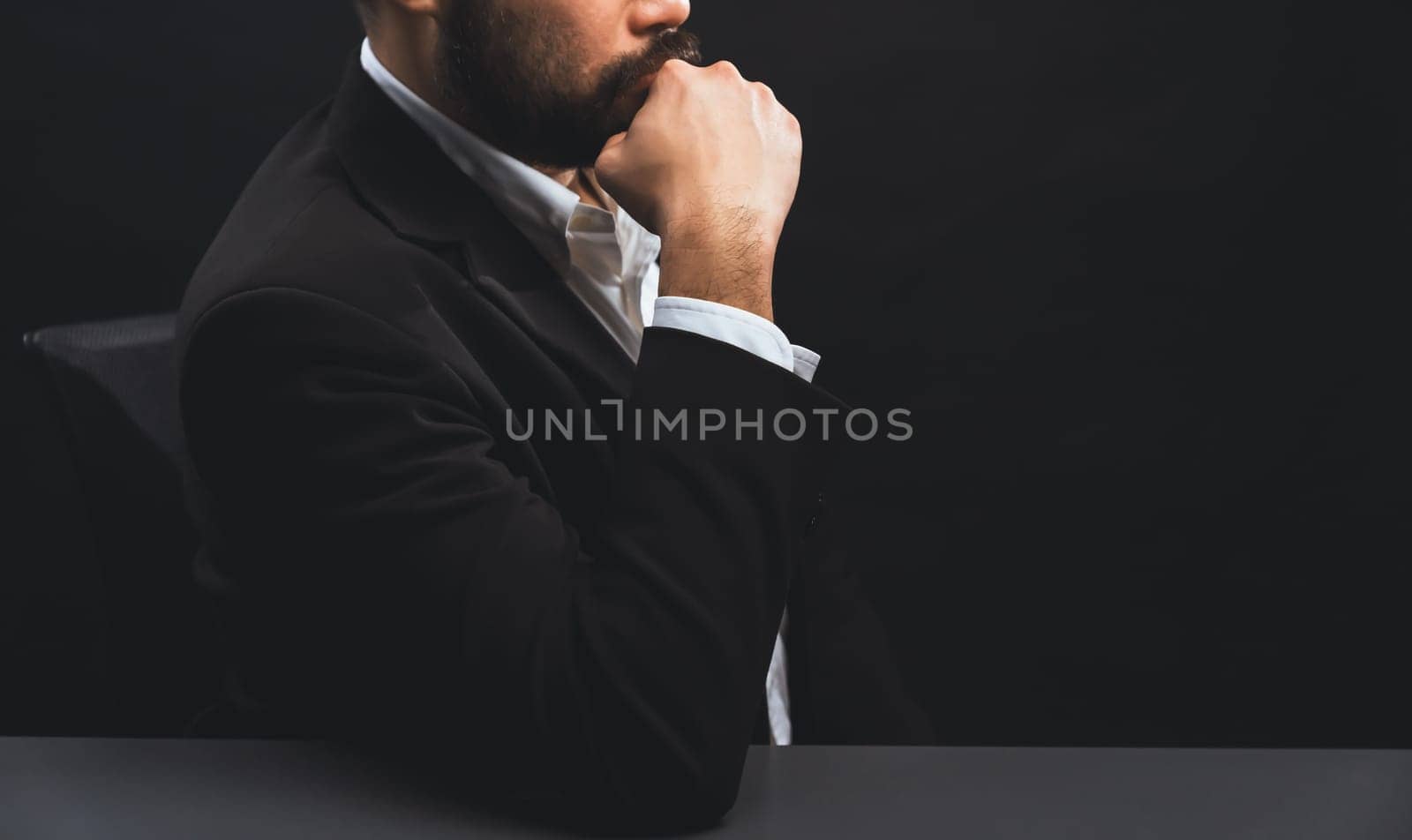 Businessman or lawyer wearing formal black suit sitting at table on isolated black background. Concept of a man with authority and seriousness gesture. equility