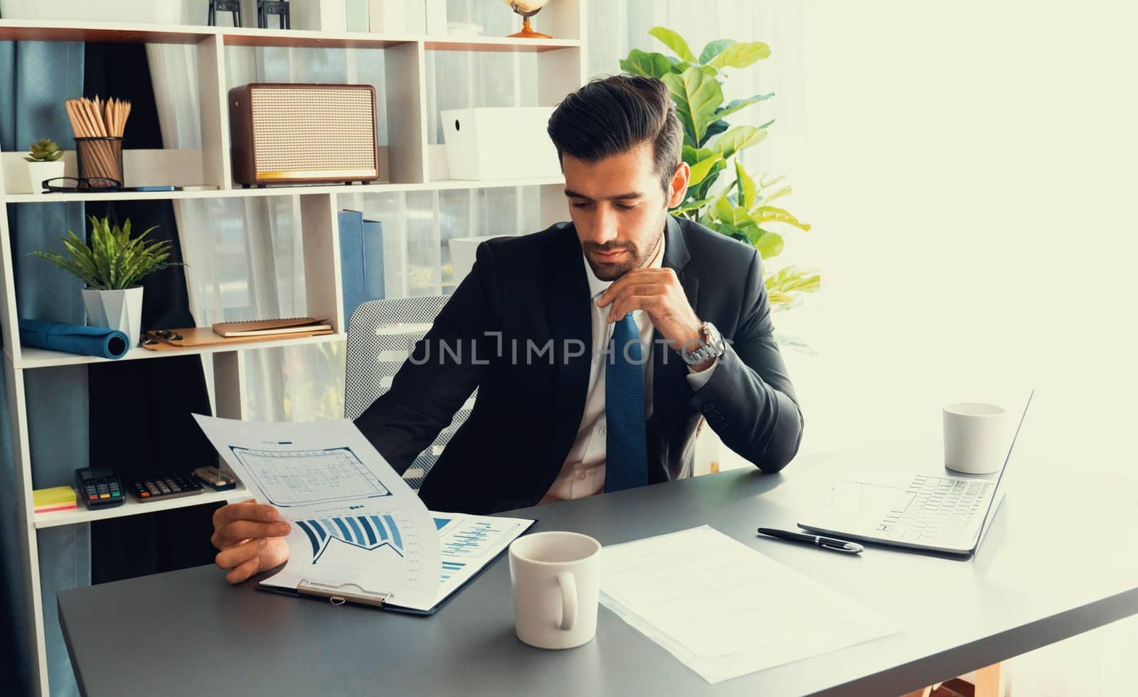 Modern professional businessman at modern office desk using laptop to work and write notes. Diligent office worker working on computer notebook in his office work space. fervent