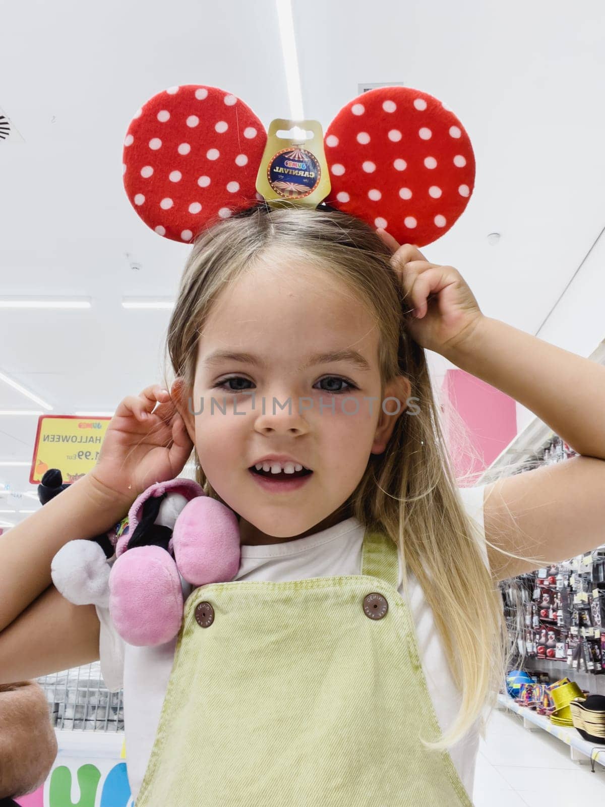 Little girl in the store trying on cute red polka dot Minnie Mouse ears. High quality photo