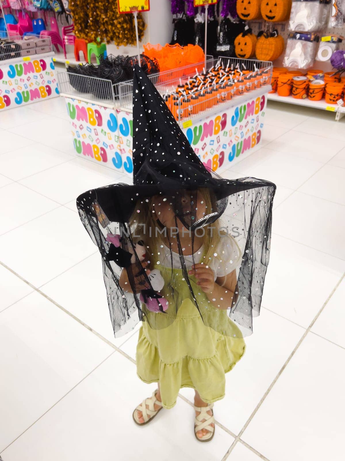Little girl tries on a pointed witch hat with a black veil in the store. High quality photo