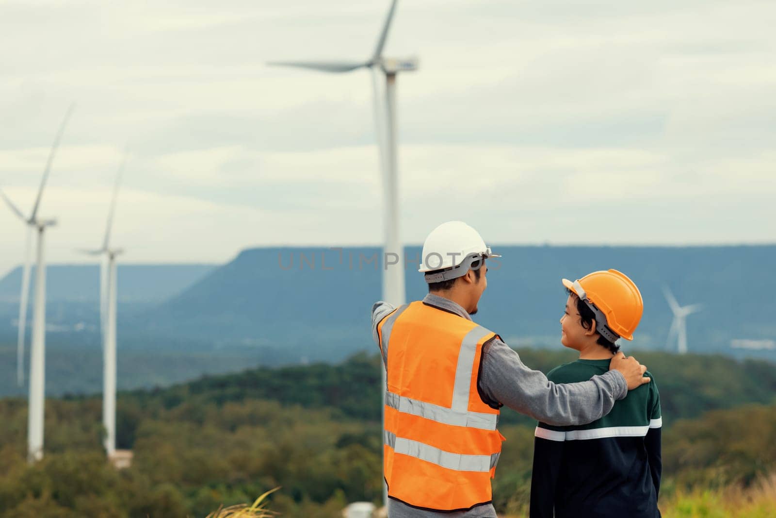 Engineer with his son on a wind farm atop a hill or mountain in the rural. Progressive ideal for the future production of renewable, sustainable energy. Energy generation from wind turbine.