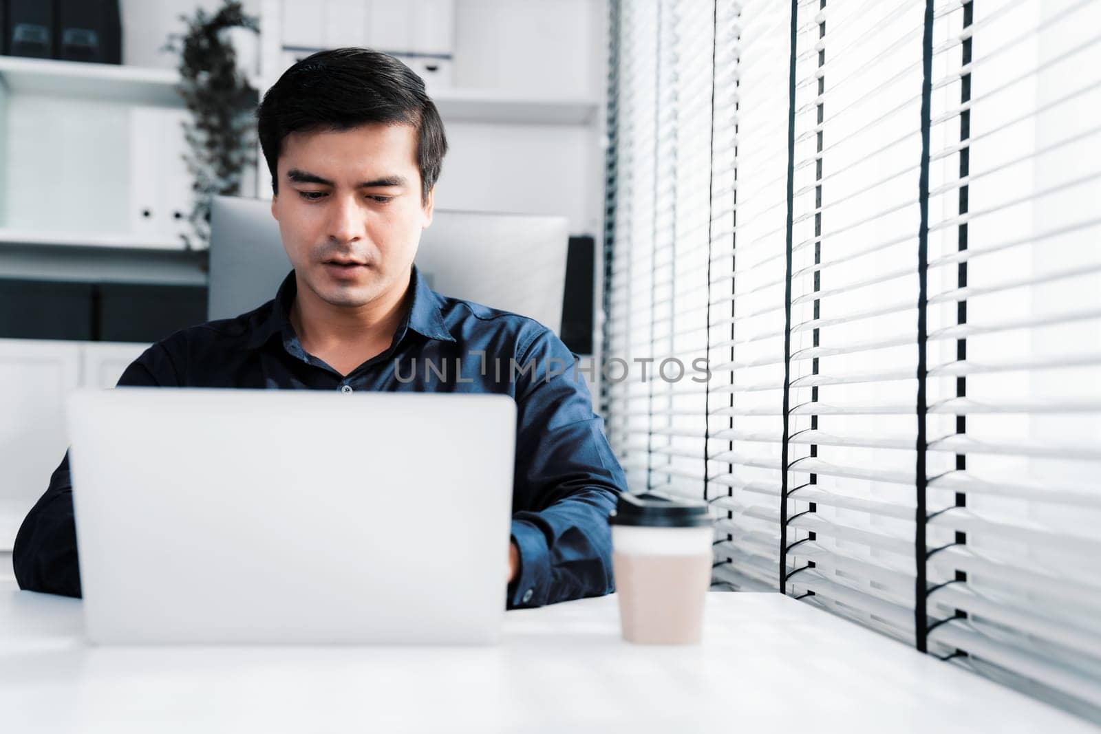 Competent male employee sits at his desk with a cup of coffee. Modern employee working with a drink, recreation during working hours, caffeine for office workers.