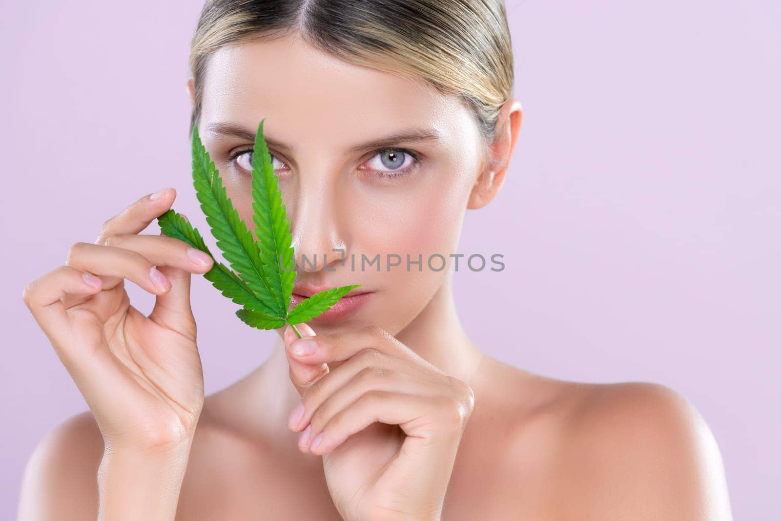Closeup alluring beautiful woman model portrait holding green leaf as concept for cannabis skincare cosmetic product for perfect skin freshness treatment in isolated pink background.
