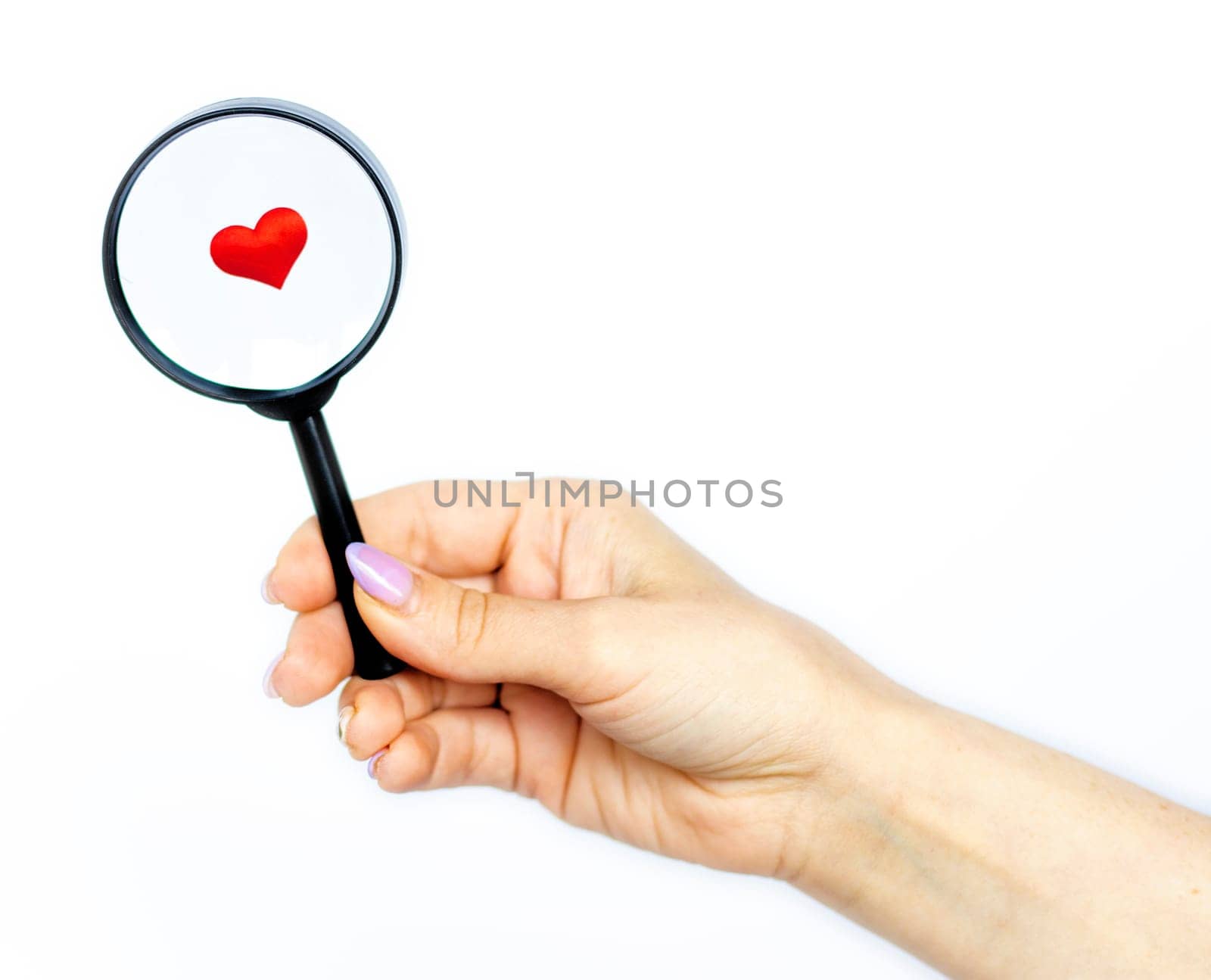 heart lies under a magnifying glass on a white background, isolate. female hand holds a magnifying glass. The concept of searching , looking for love, love background. romantic minimalism background