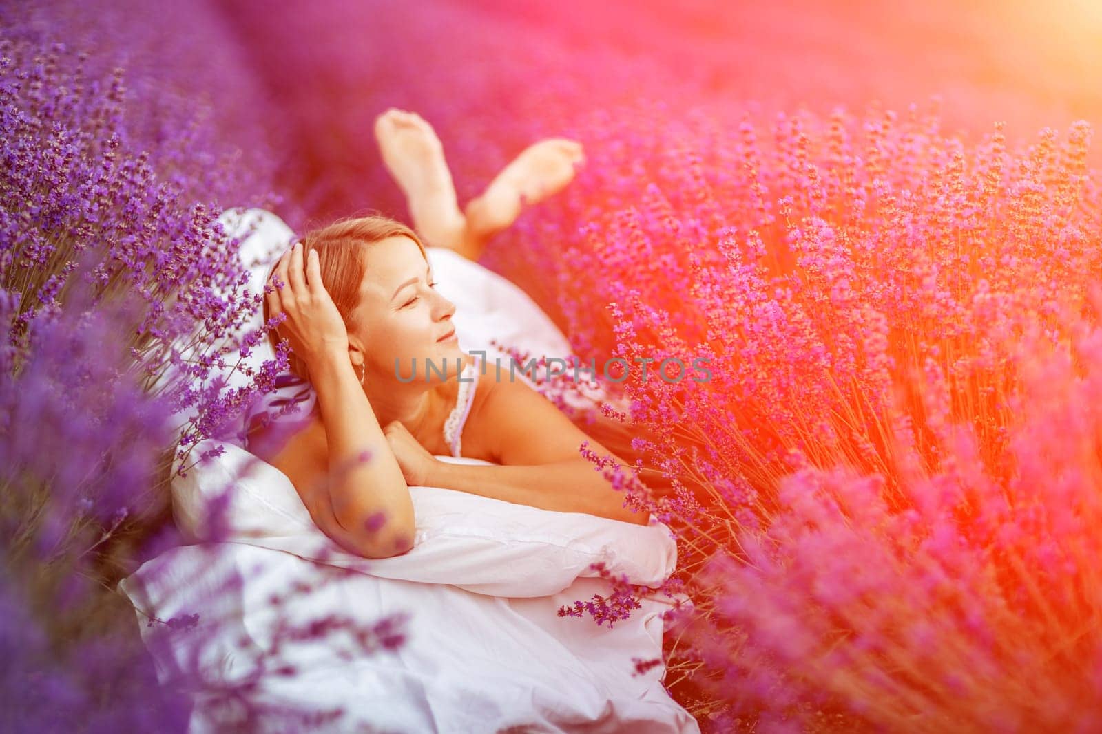 A middle-aged woman lies in a lavender field and enjoys aromatherapy. Aromatherapy concept, lavender oil, photo session in lavender.