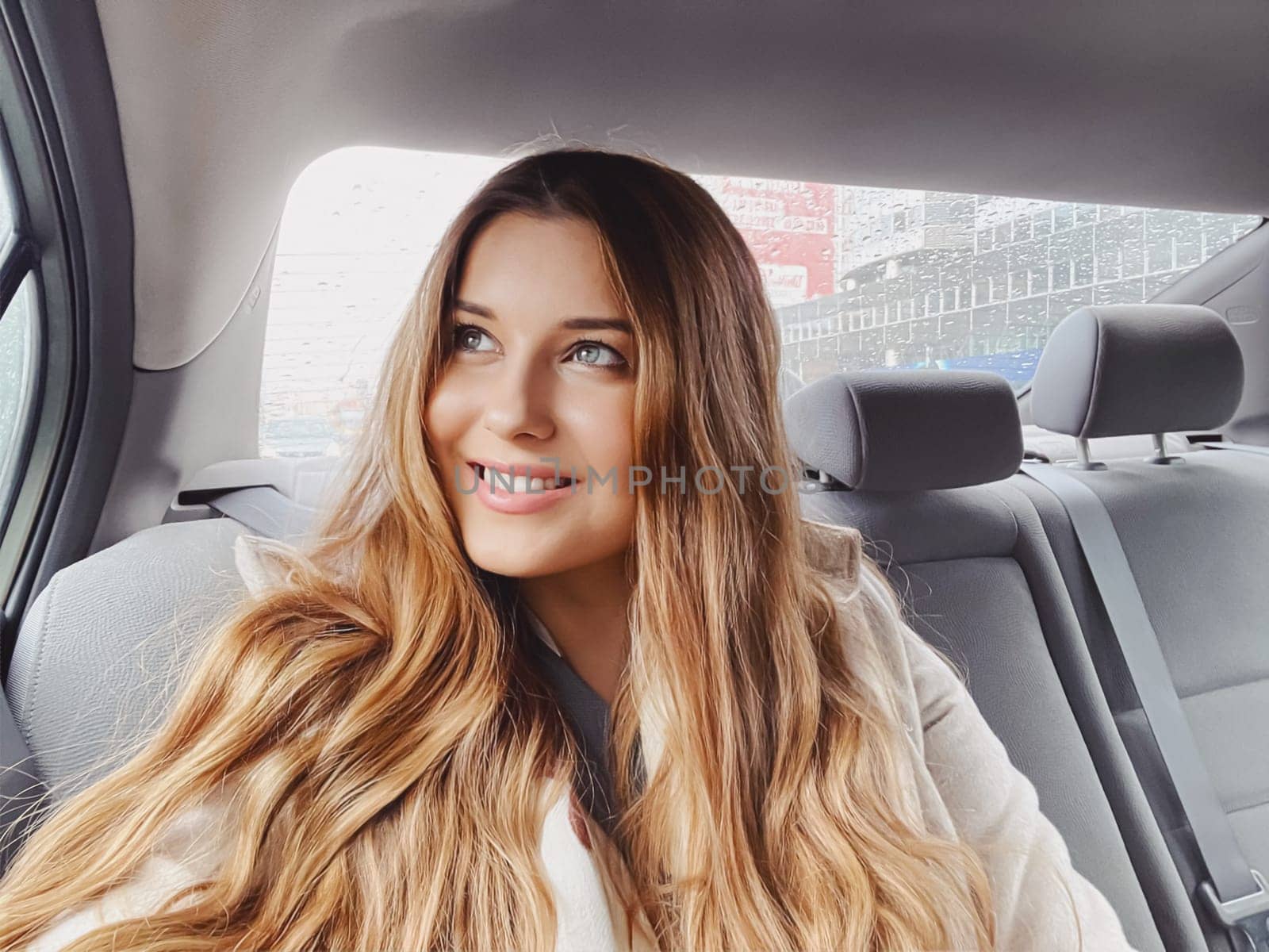 Happy young woman in the car looking out the window, exploring the city, taxi service and travel.