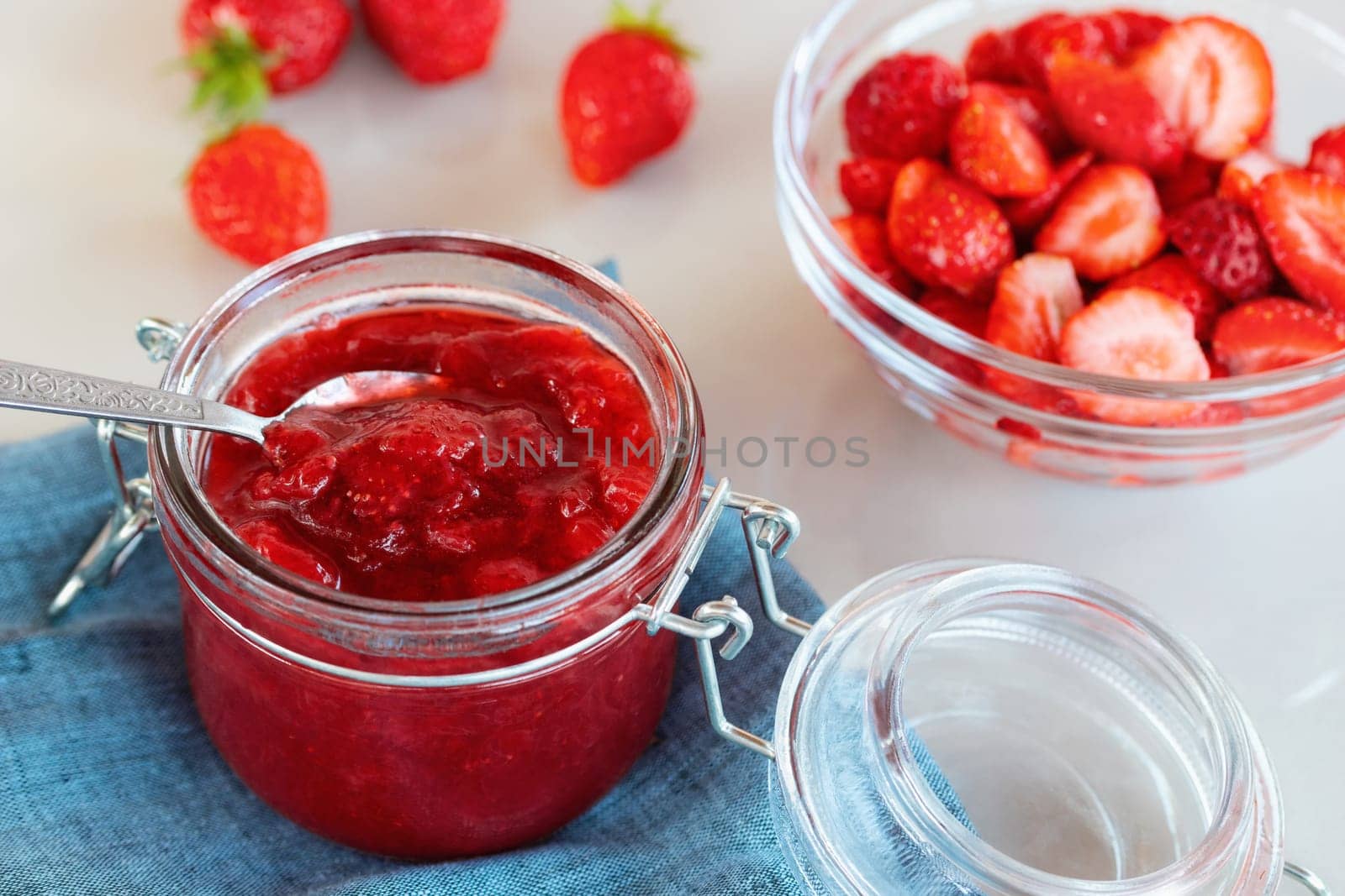 Glass jar with strawberry jam prepared for canning and fresh strawberries in a bowl on the table by galsand