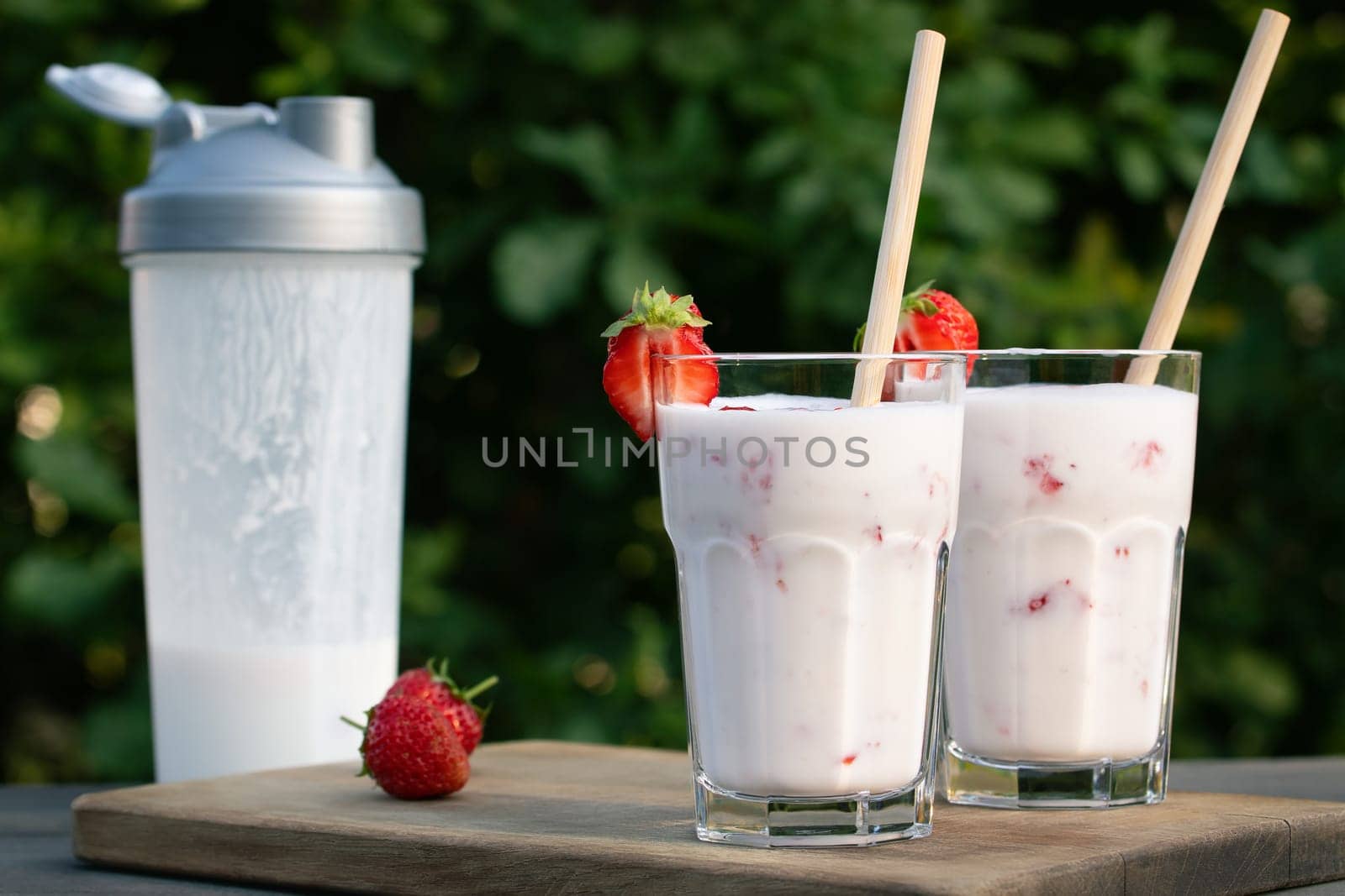 Protein shake from yogurt and strawberries in a shaker and two glass glasses on a wooden table.