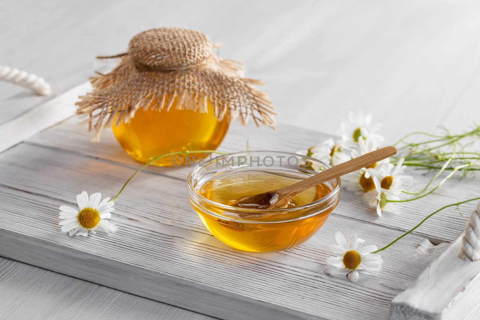 Chamomile syrup in a small bowl and in a jar on a white wooden table.