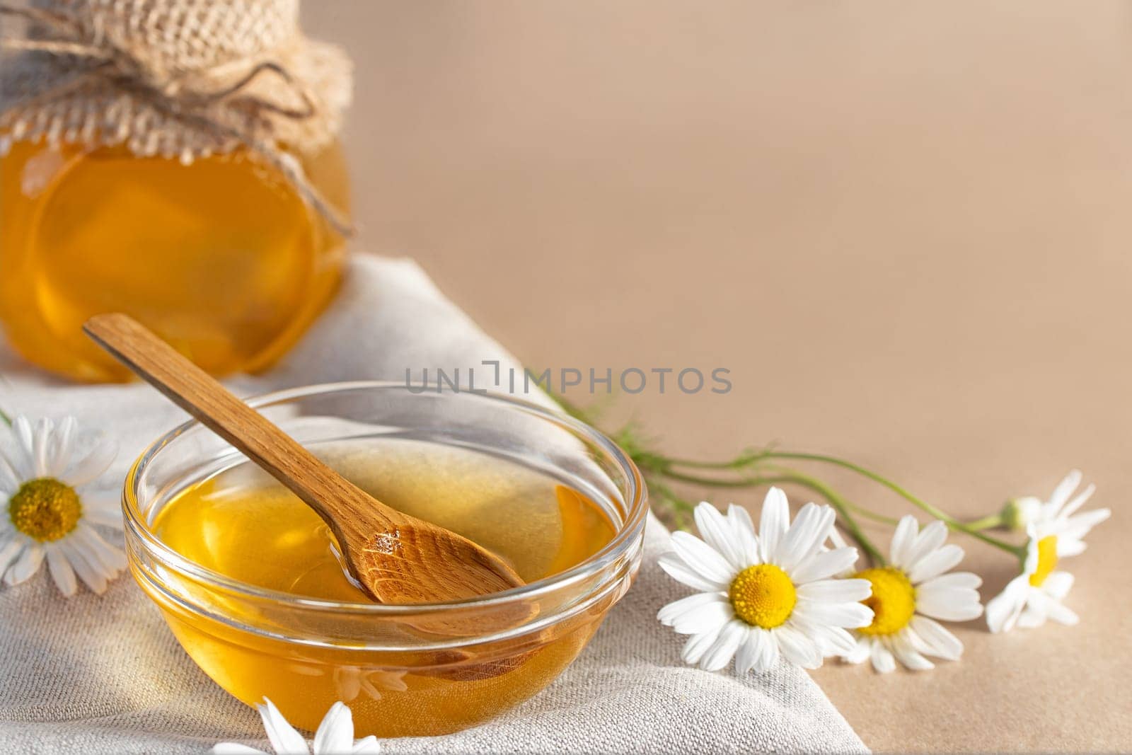 Chamomile syrup in a small bowl and in a jar and chamomile flowers on a linen kitchen towel, copy space.