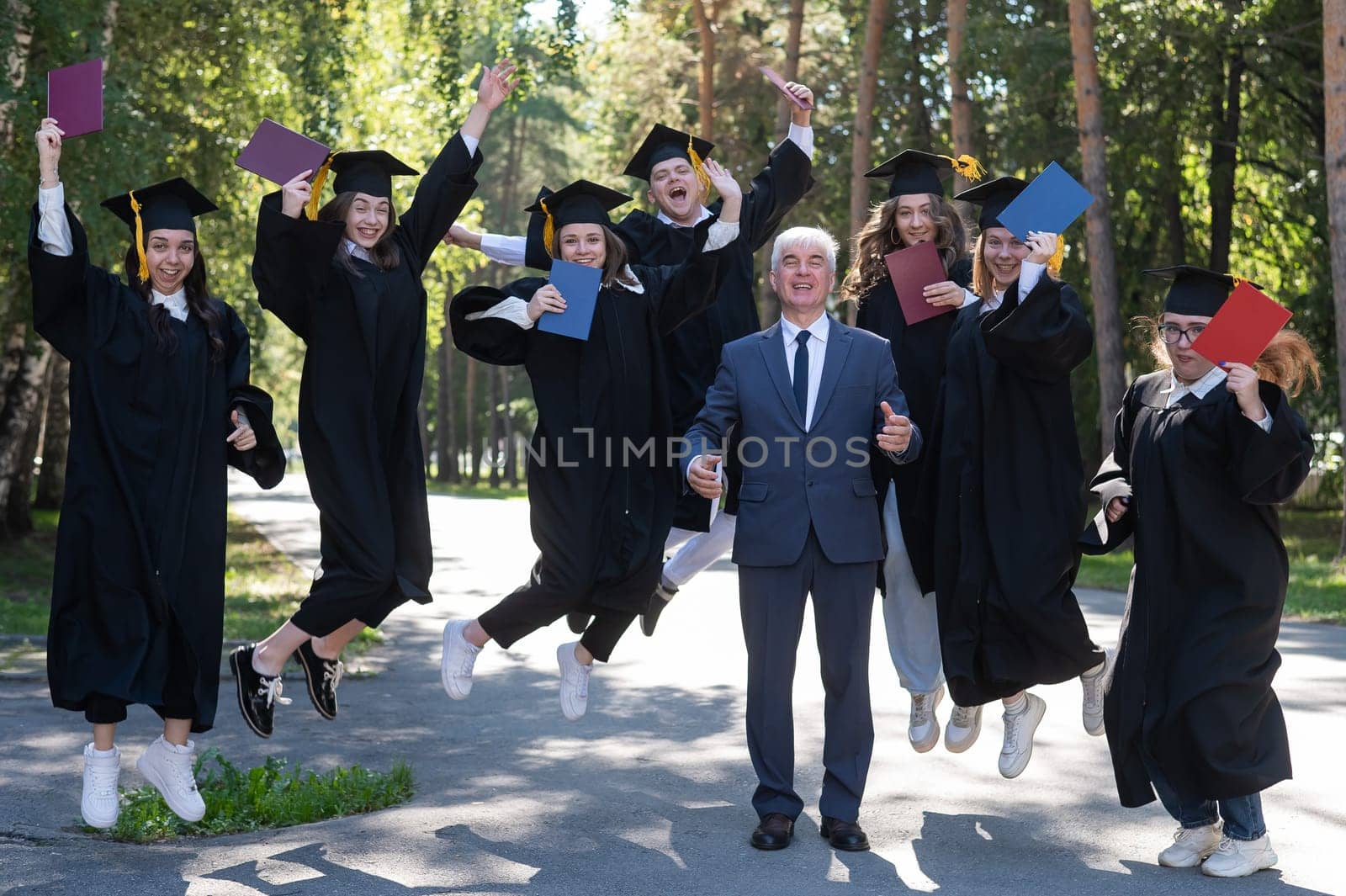 A university professor and seven robed graduates are jumping outdoors