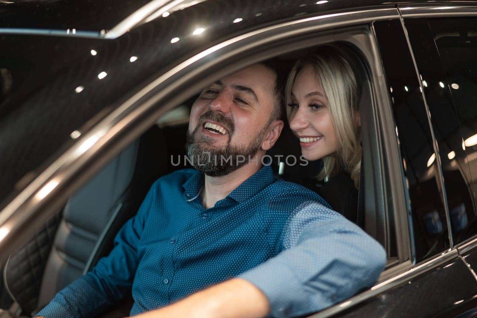 Happy married couple testing new car in car showroom