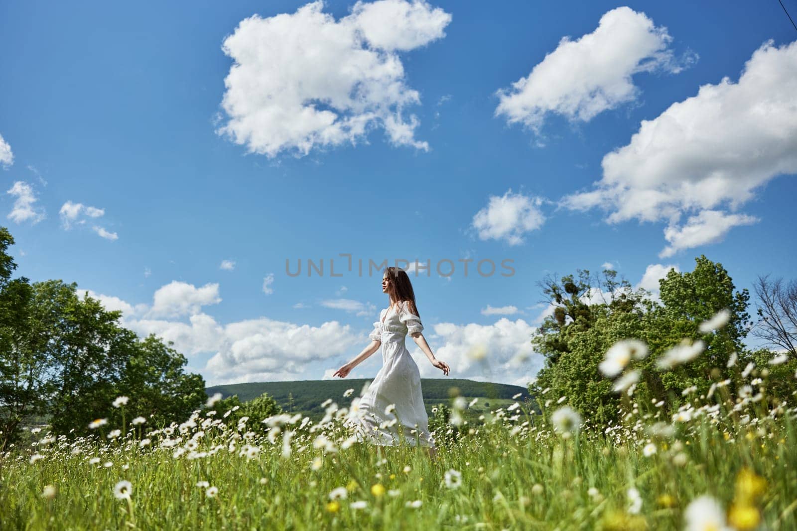 a woman in a light dress runs far across a chamomile field against a blue sky, enjoying harmony with nature. High quality photo