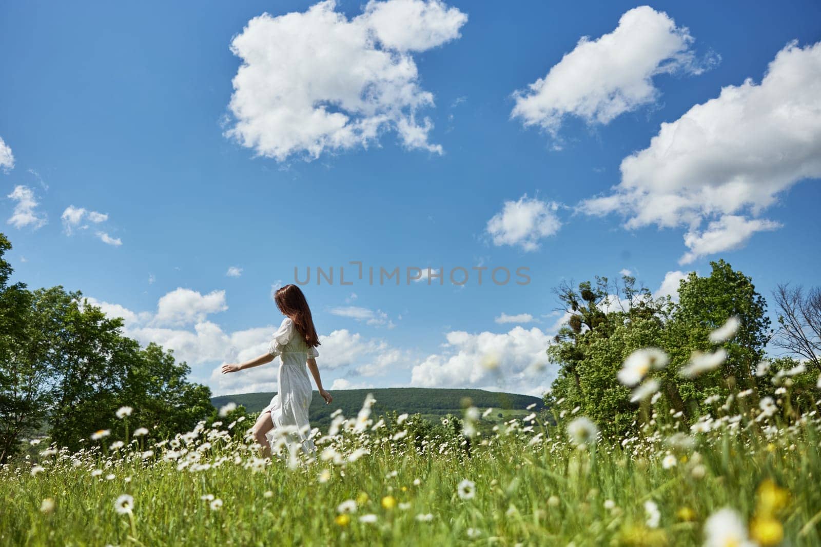 a woman in a light dress runs far across a chamomile field against a blue sky, enjoying harmony with nature by Vichizh