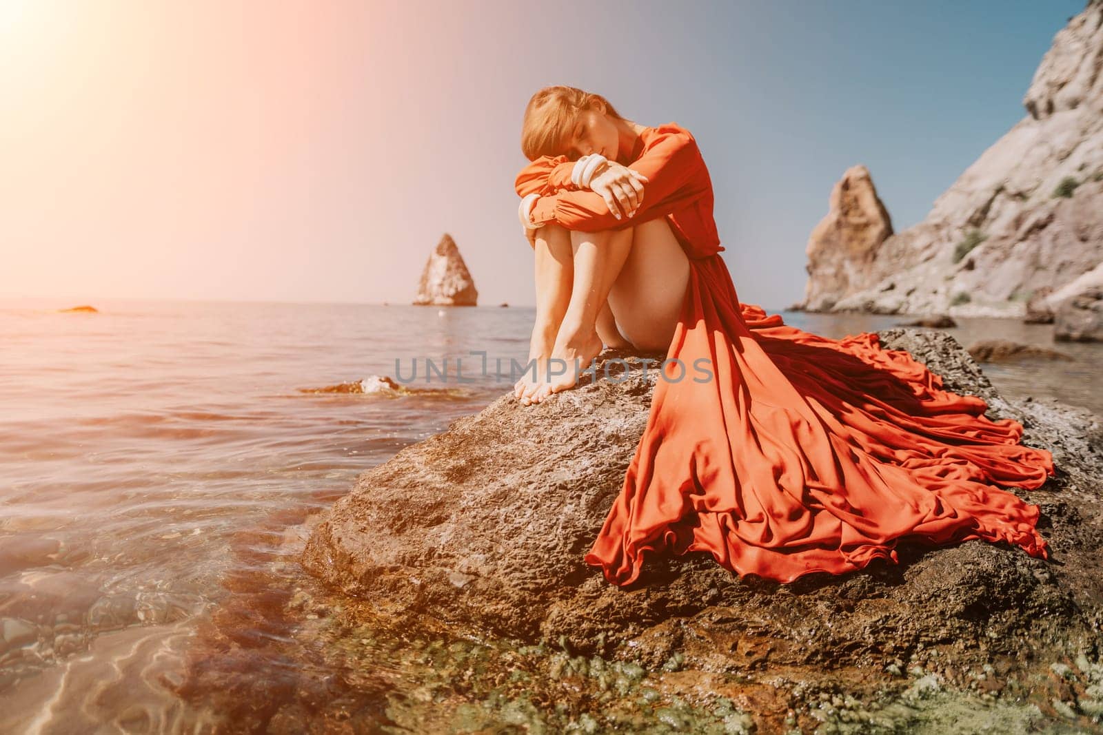 Woman travel sea. Happy tourist in red dress enjoy taking picture outdoors for memories. Woman traveler posing on the rock at sea bay surrounded by volcanic mountains, sharing travel adventure journey by panophotograph