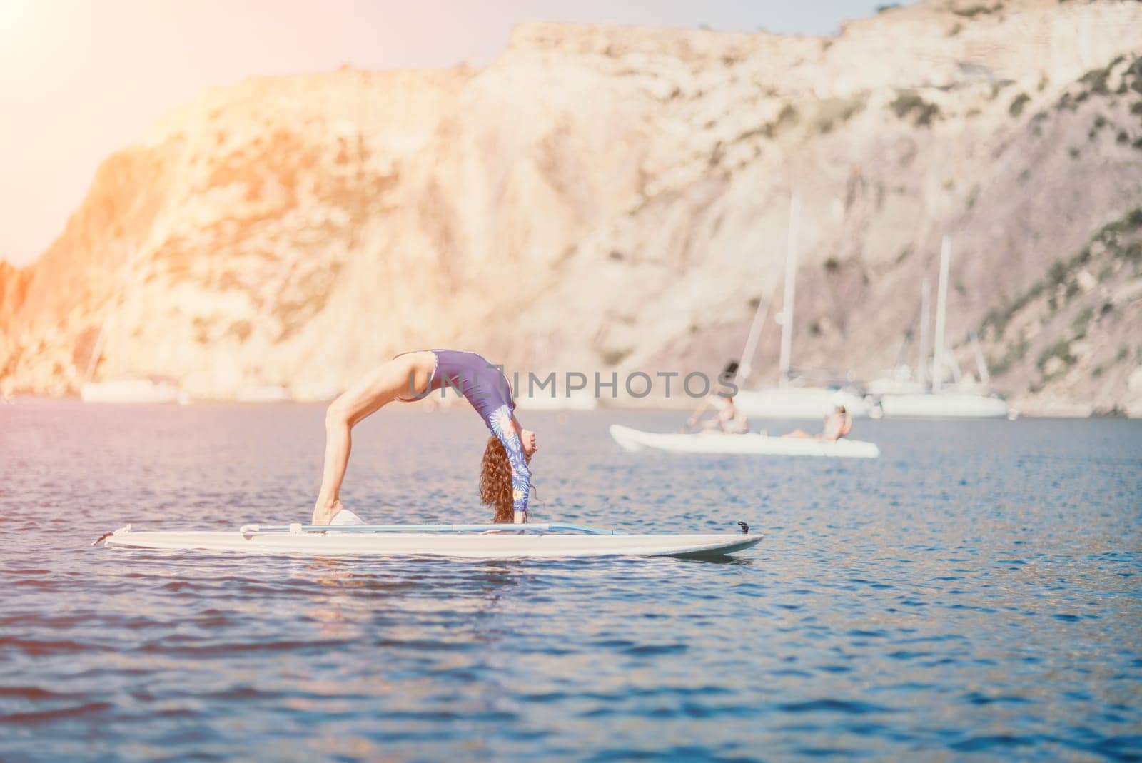 Woman sup yoga. Middle age sporty woman practising yoga pilates on paddle sup surfboard. Female stretching doing workout on sea water. Modern individual female hipster outdoor summer sport activity. by panophotograph