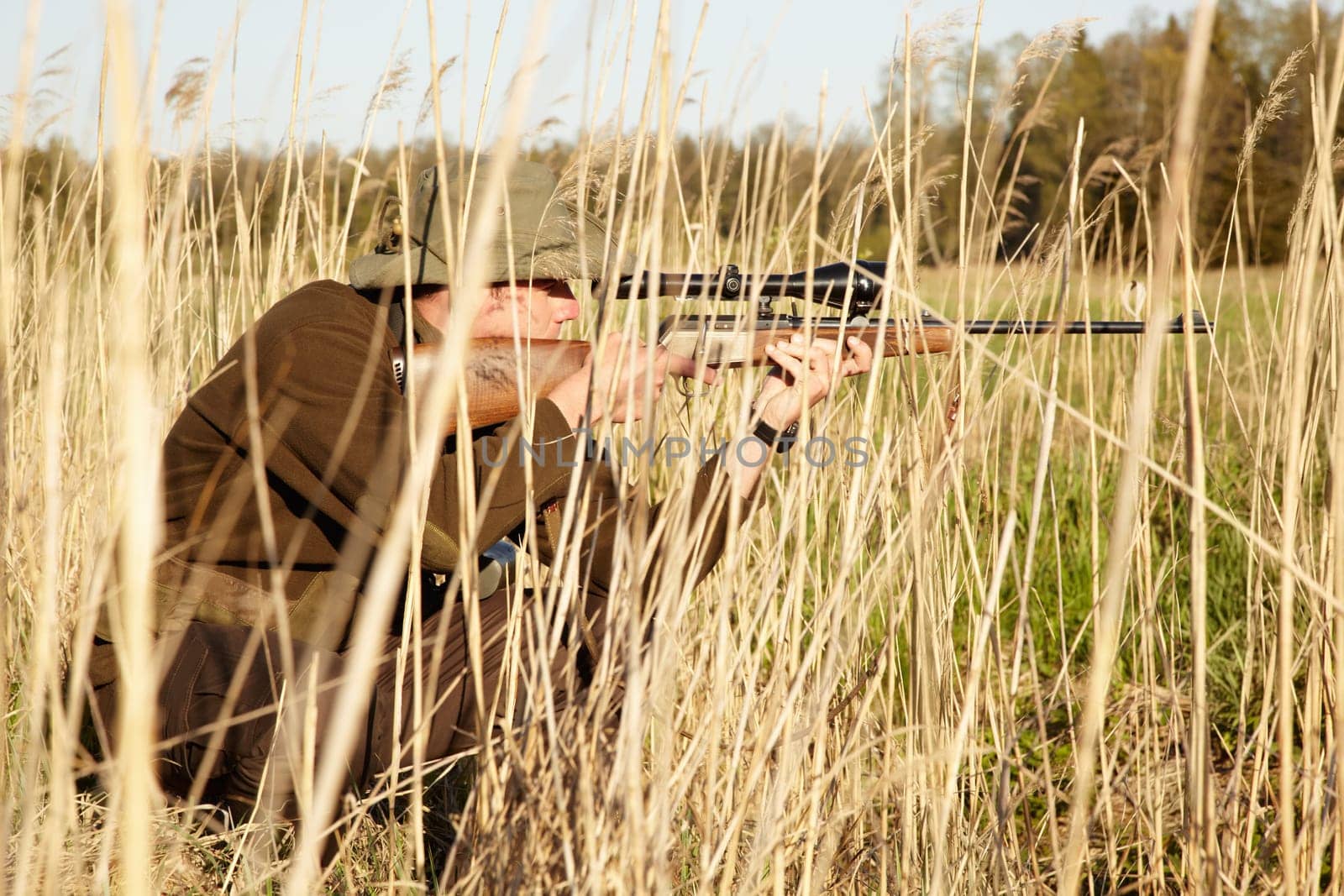 Nature, hunter and man with a rifle while in camouflage shooting in outdoor field. Grass, wildlife and male sniper hunting animals with shotgun weapon hiding in plants to shoot target in countryside
