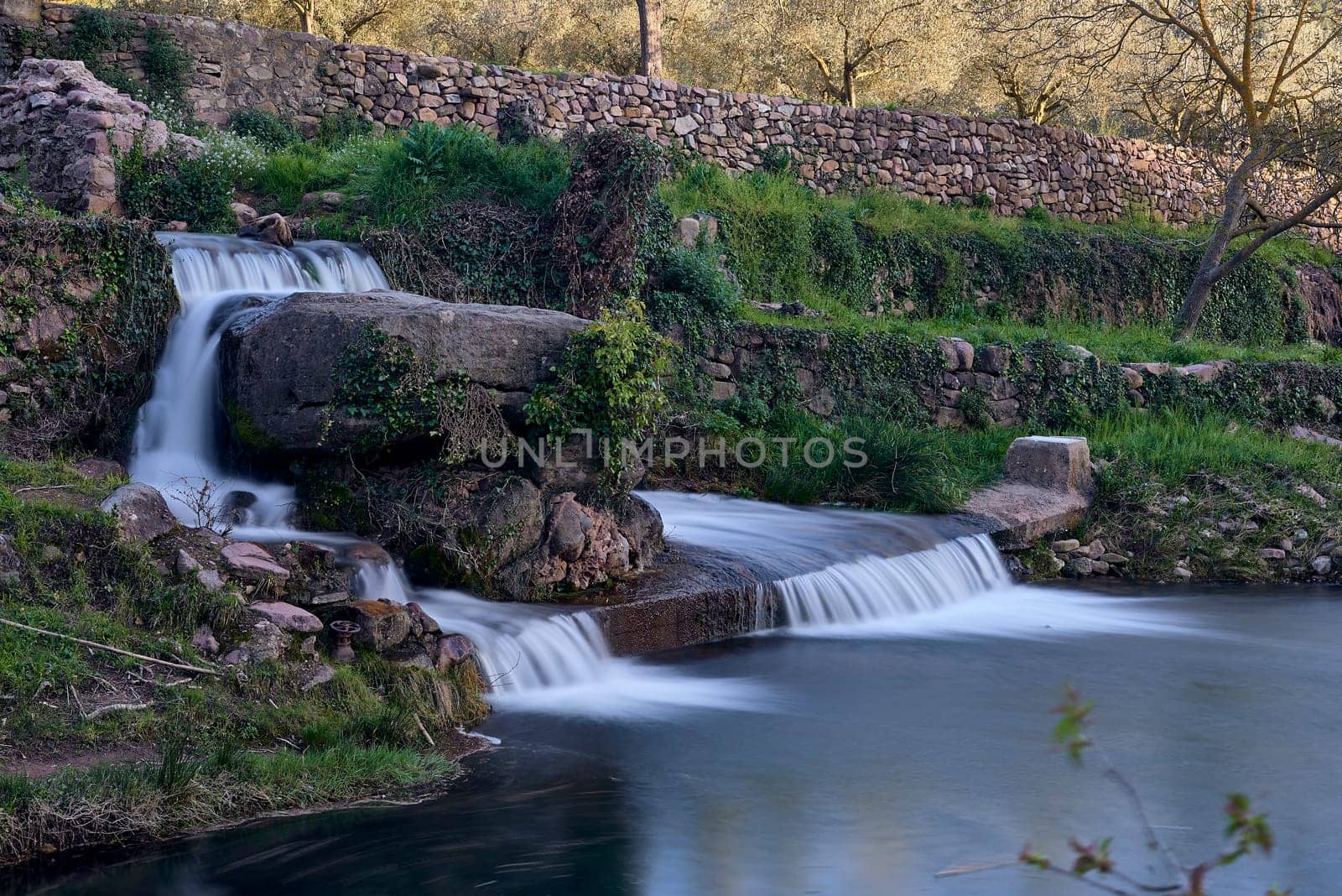 Small waterfalls in a mountain stream on a sunny day.long exposure. Mystic, vegetation, stone walls, lonely, empty space, romantic, idyllic.