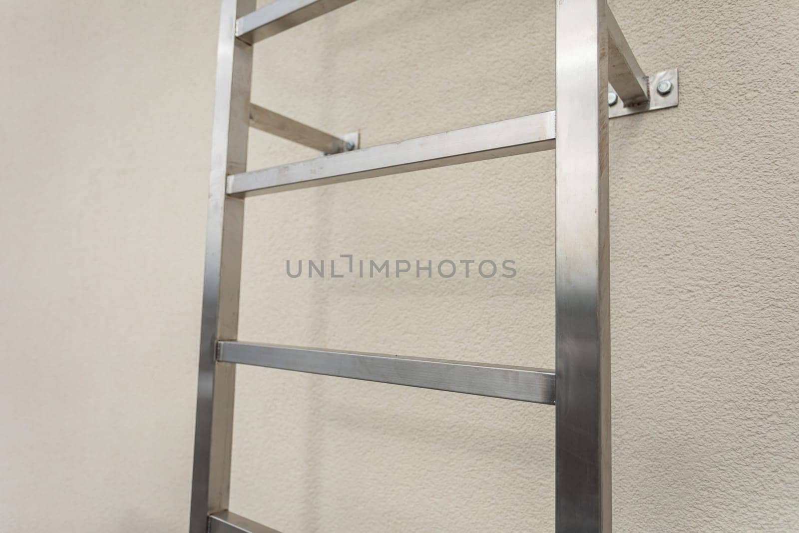 Close-up view of a section of a stainless steel ladder mounted on a building wall. Square stainless steel section.