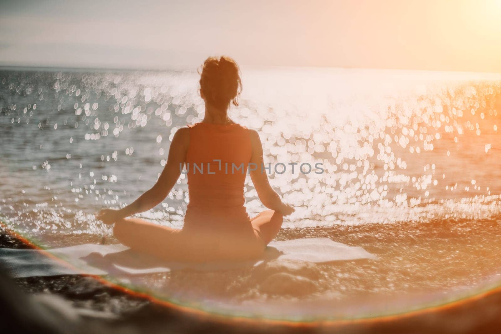 The woman in a red suit practicing yoga on stone at sunrise near the sea. Young beautiful girl in a red bathing suit sits on the seashore in lotus position. Yoga. Healthy lifestyle. Meditation