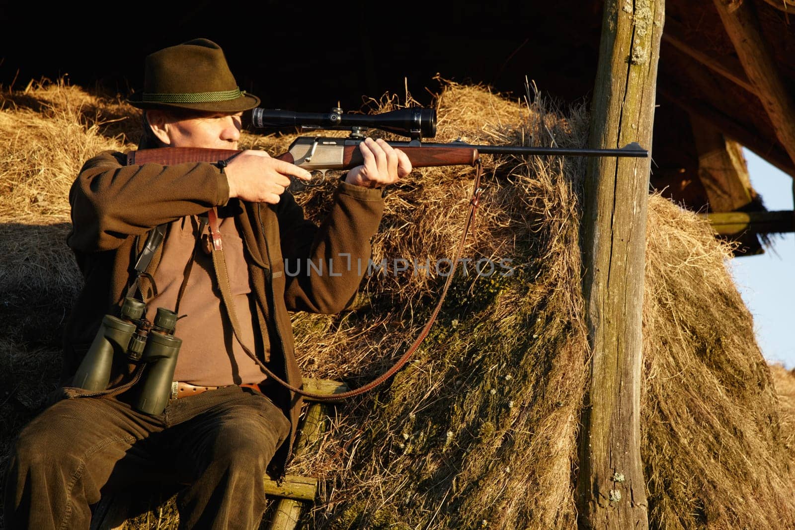 Hunter, safari gun and man shooting with aim at sunrise at a wildlife lookout for hunting. Target, weapon and game sports of a male person outdoor in nature with a gun to shoot wild and animals by YuriArcurs