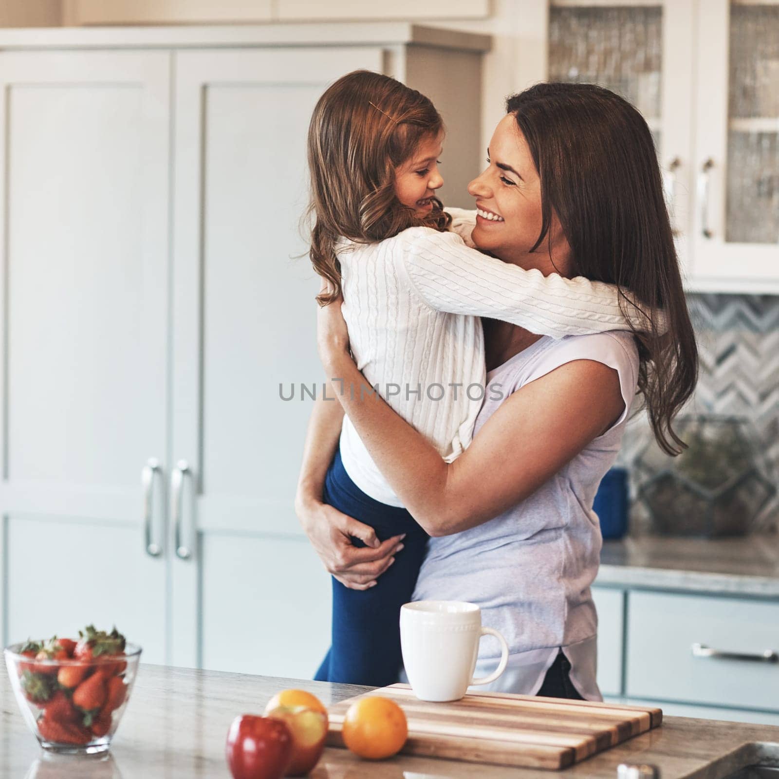Youre the apple of my eye. a happy mother hugging her cute little girl in the kitchen at home. by YuriArcurs